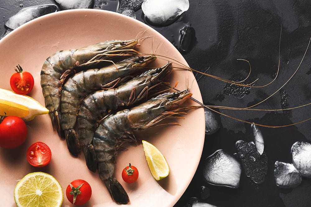 Raw shrimps with lemon on black background