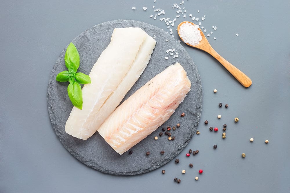 Fresh raw cod fillet with spices, pepper, salt, basil on stone p