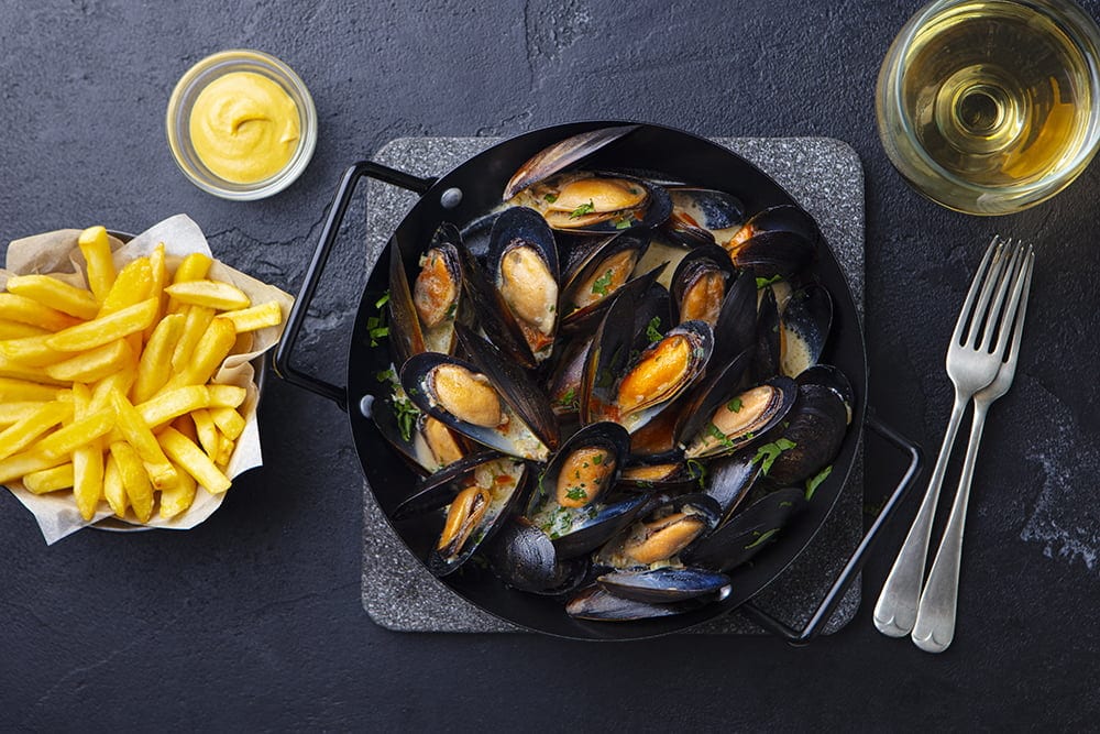 Mussels with french fries and white wine in cooking pan. Grey background. Top view.